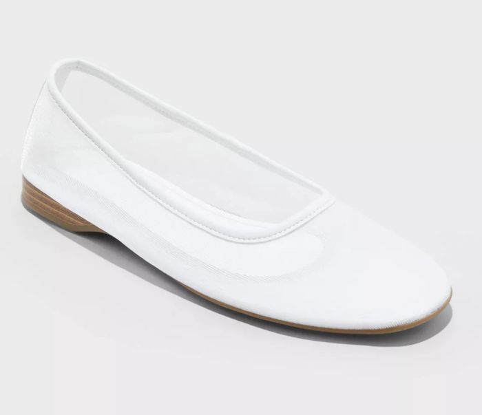 A white ballet flat shoe featuring a small heel and round toe
