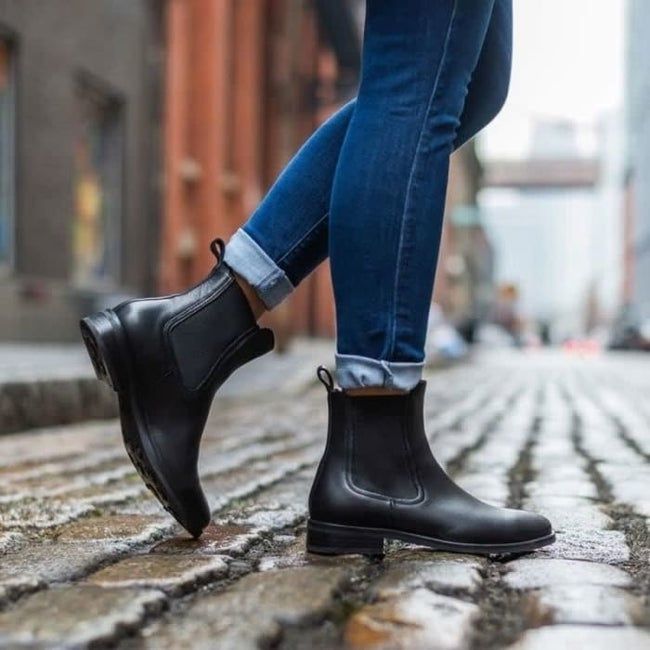 A model showcasing the black booties while strolling across a cobblestone street.
