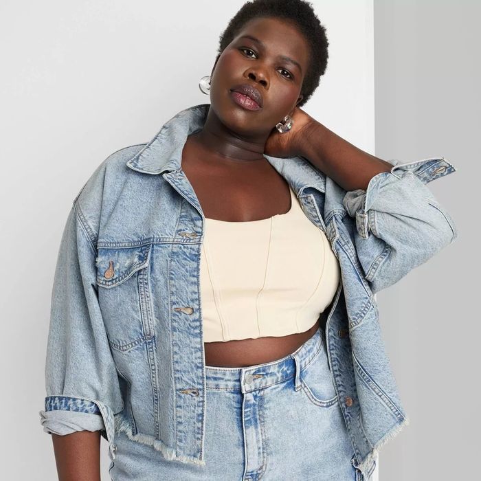 A model wearing a light-wash denim jacket over a crop top and high-waisted denim shorts