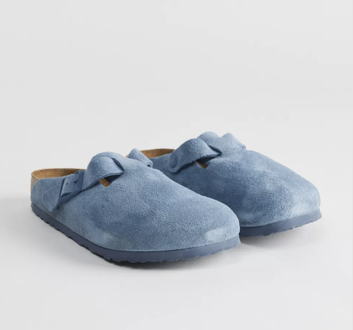 Blue suede clogs featuring cork insoles and a bow detail on top. The textured sole ensures excellent grip, making them ideal for casual outings or relaxing at home.