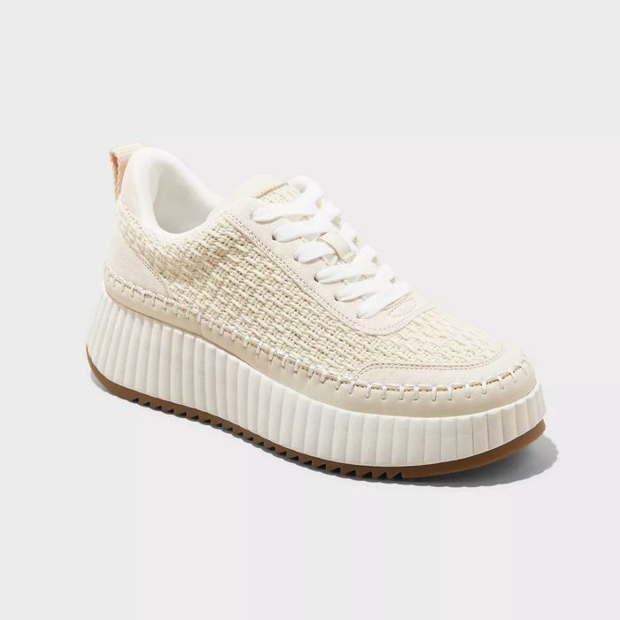 A cream-colored knitted sneaker with a ribbed sole, displayed against a plain background