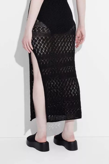 A person wearing a black textured skirt and chunky platform shoes, posing against a white backdrop