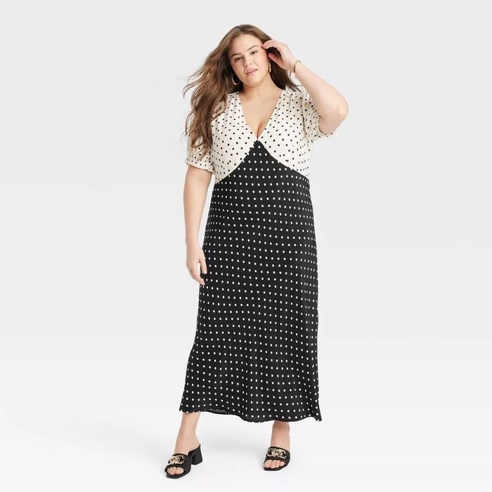 A model wearing a polka-dot short-sleeve dress and sandals, posing for a catalog shoot