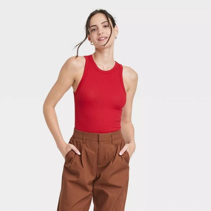 A model wearing a high-neck red ribbed tank top paired with brown pants