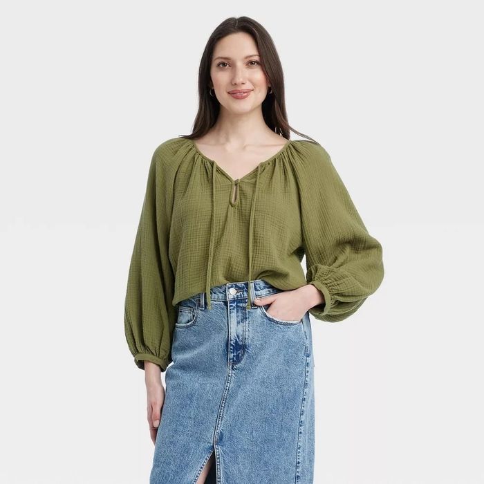 A model wearing an olive green long-sleeve blouse with a V-neckline, paired with a light blue denim skirt featuring a front slit