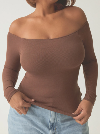 A person styled in an off-shoulder, long-sleeved top paired with classic denim jeans.
