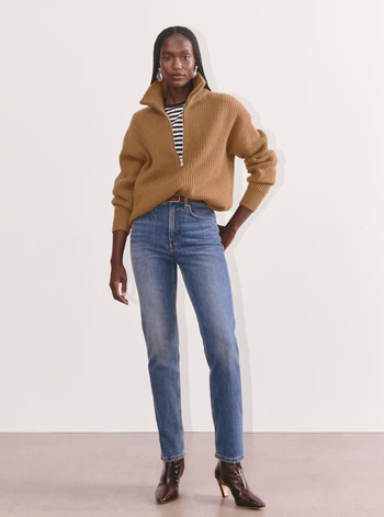 A model wearing a textured sweater over a striped top, paired with blue jeans and heeled boots, featured in a shopping context.