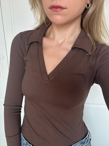 A person dressed in a fitted, long-sleeve brown V-neck shirt.