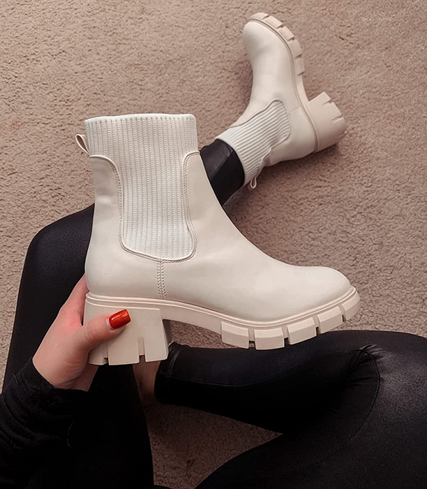 reviewer holding one beige boot while wearing the other