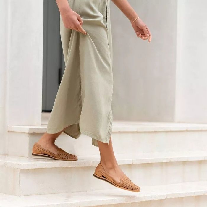 A person in wide-leg trousers and tan woven flats stepping up the stairs, exemplifying a relaxed and effortless fashion vibe
