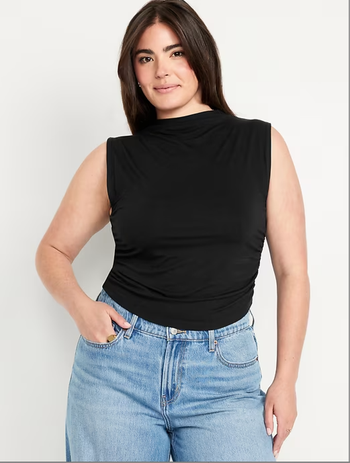 A model wearing a sleeveless black top paired with jeans.