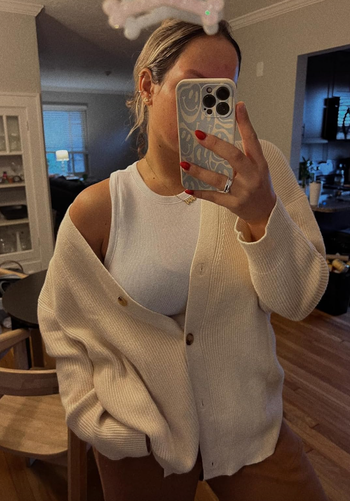 A reviewer showcasing a white cardigan.