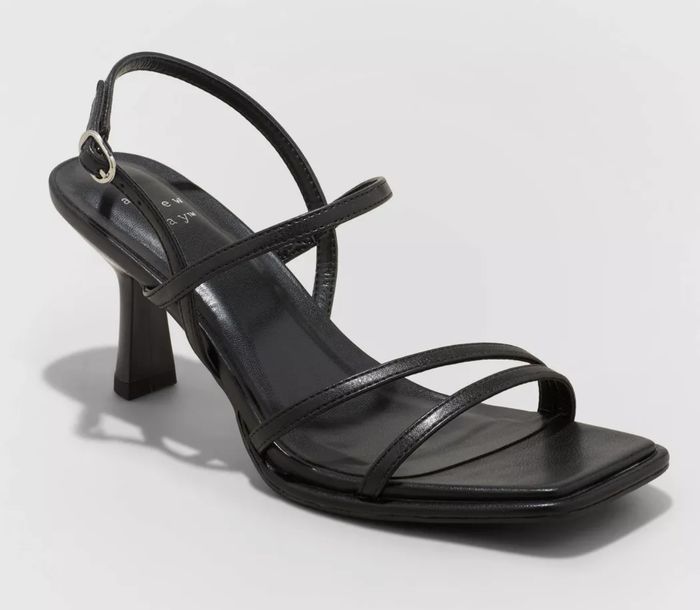 Black heeled sandals with straps and a circular buckle detail set against a white background