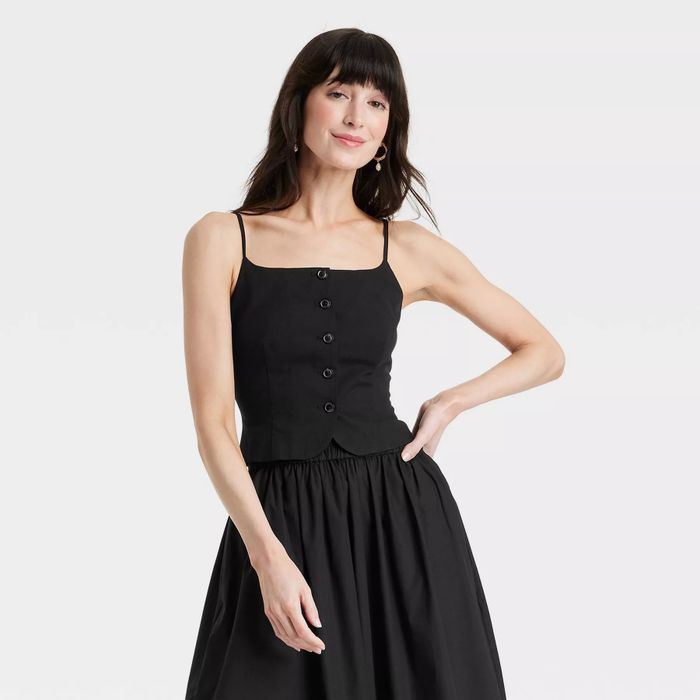 A model dressed in a sleeveless, button-up black top paired with a matching black skirt