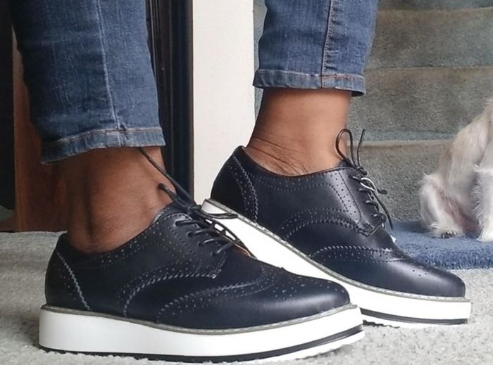 A reviewer wearing jeans and navy platform oxfords, with a dog in the background