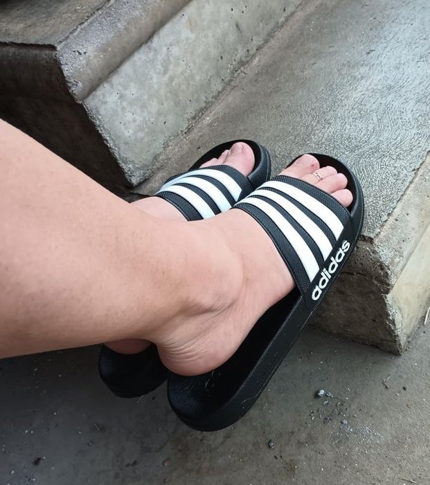 A reviewer wearing black and white striped Adidas slides on a concrete step