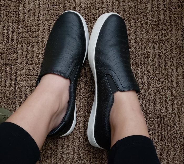 A reviewer wearing black sneakers with a snakeskin print