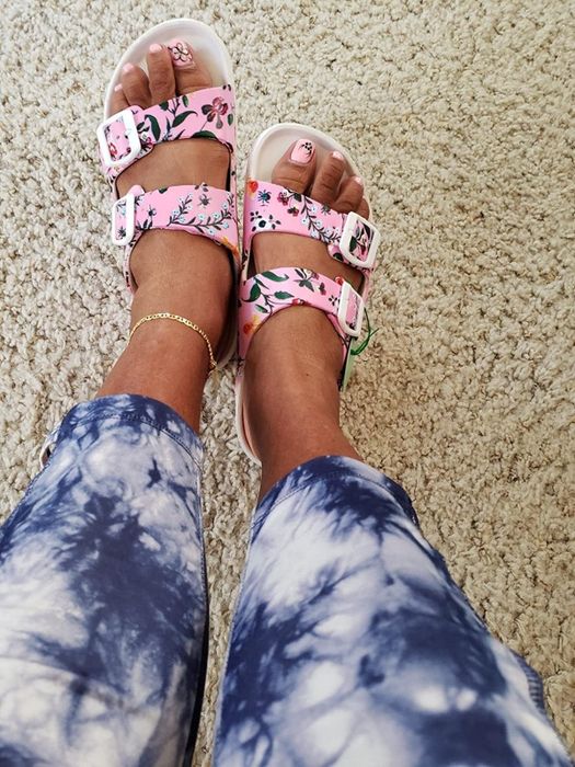 A reviewer wearing the same slides in a pink shade with a pink and white floral pattern