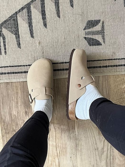 A reviewer displaying the top and side views of the beige clogs