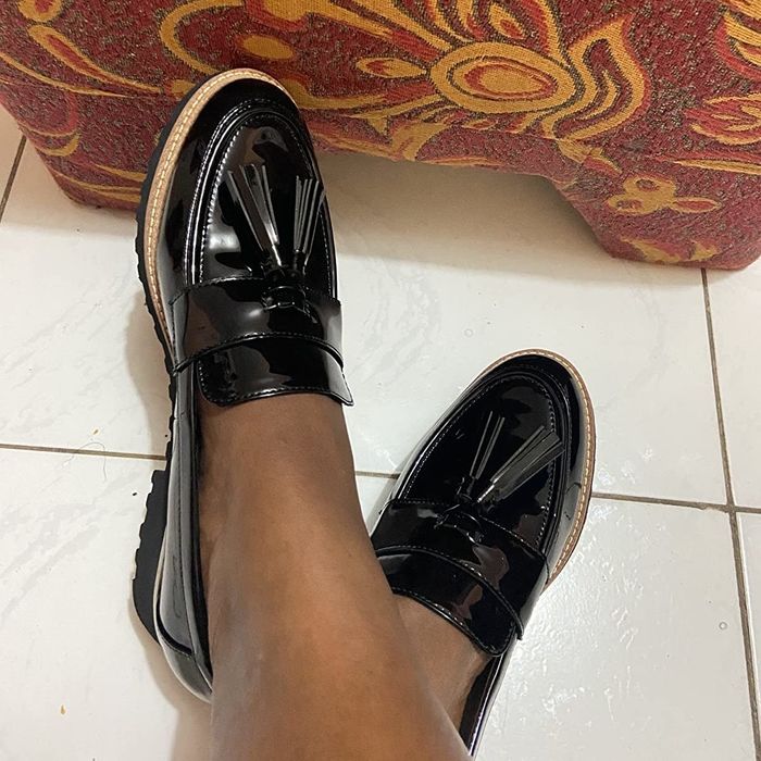 A photo taken by a reviewer showcasing a pair of feet wearing black patent loafers with tassels at the toe area.
