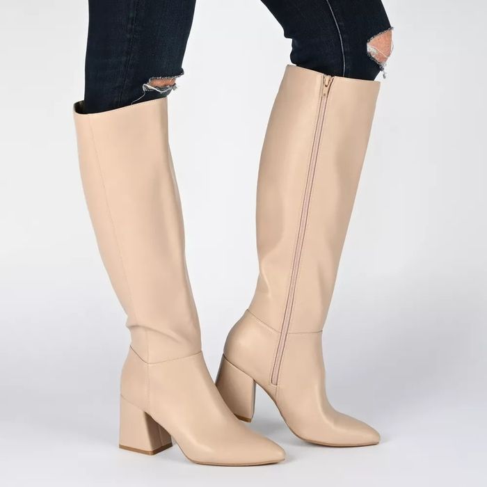 A model sporting ripped denim paired with beige knee-high boots showcasing block heels and a zipper detail