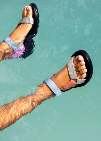 Two legs floating in water wearing Teva sandals, showcasing their suitability for aquatic activities