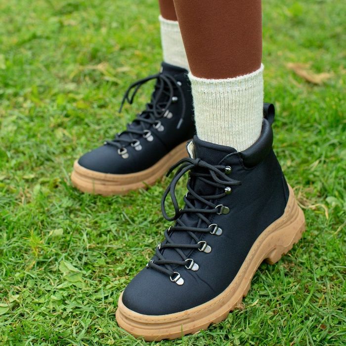 A close-up of a model wearing black lace-up boots with a tan lug sole