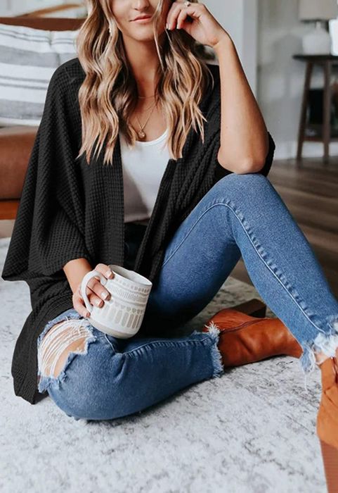 Model dressed in a black poncho featuring a chunky-knit pattern