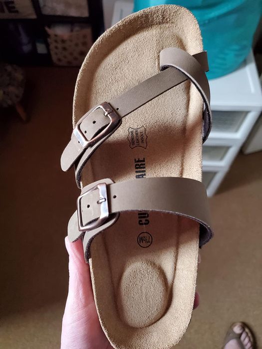 A reviewer holding up the tan sandal to highlight its supportive footbed