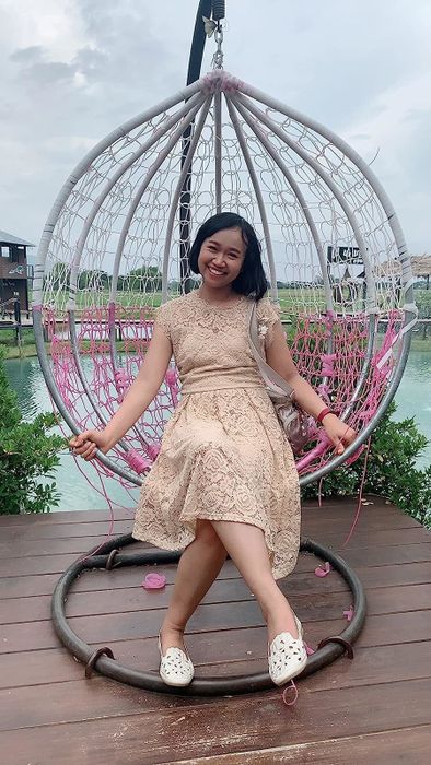 reviewer sitting in an egg chair, wearing white flower flats with a lace dress