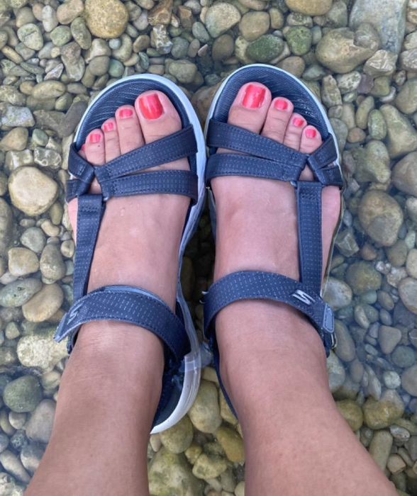 A reviewer wearing the dark gray sandals on a rocky surface