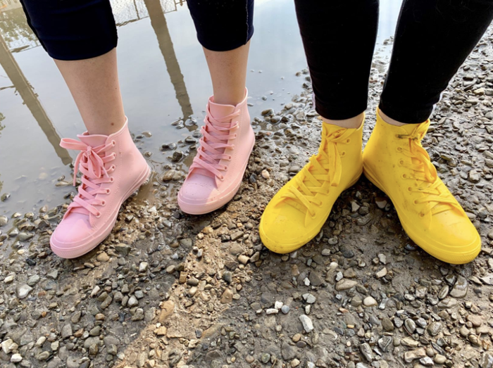 two reviewers showcasing high-top sneaker-style rain shoes in light blue and yellow