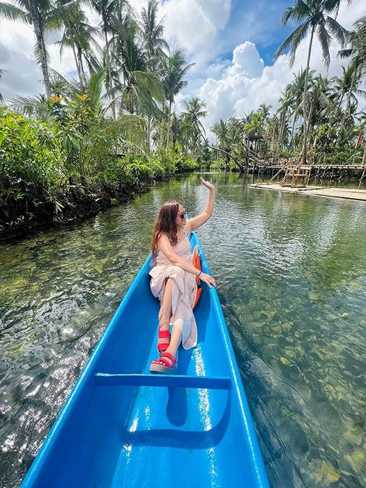 same reviewer in red wedge sandals waving from a boat on a tropical lake