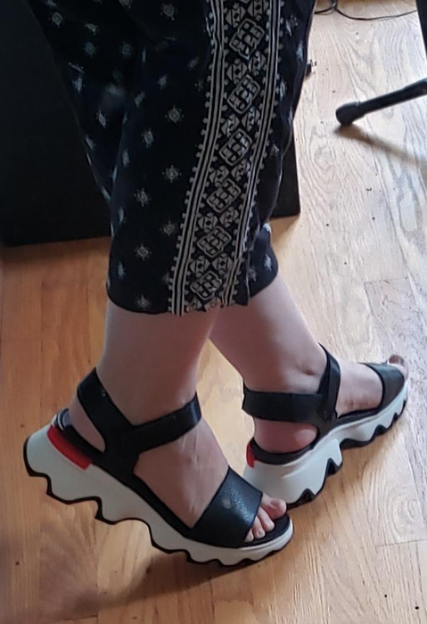 A close-up photo of a reviewer's black strappy sandals with white soles