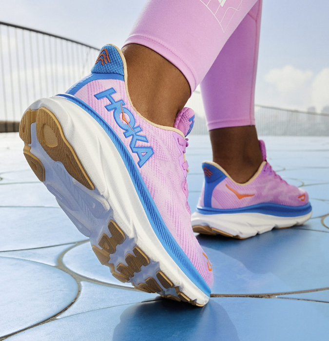 a model wearing the lilac shoes with a blue Hoka logo
