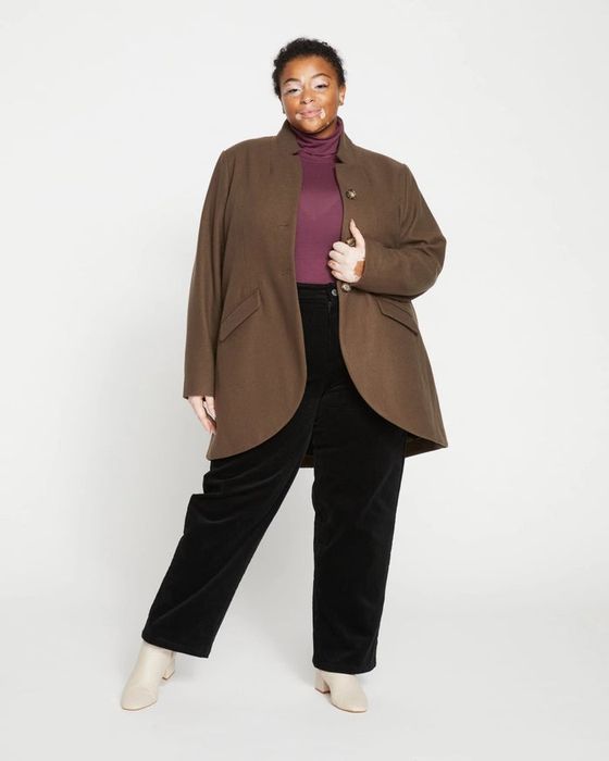 A model dressed in a brown coat paired with a black and red outfit and white shoes
