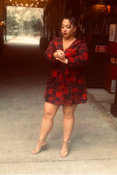 A reviewer wearing a long-sleeve black dress adorned with vibrant red roses