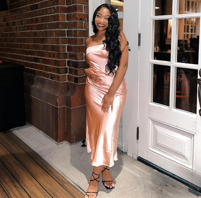 A reviewer in an elegant satin dress strikes a pose by a brick wall, offering perfect inspiration for evening wear shopping.