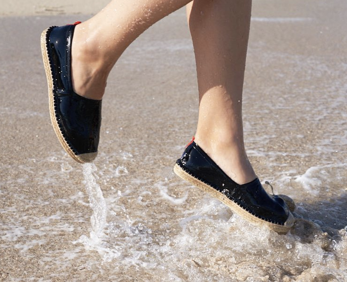 a model wearing the espadrilles while jumping in the water at the beach