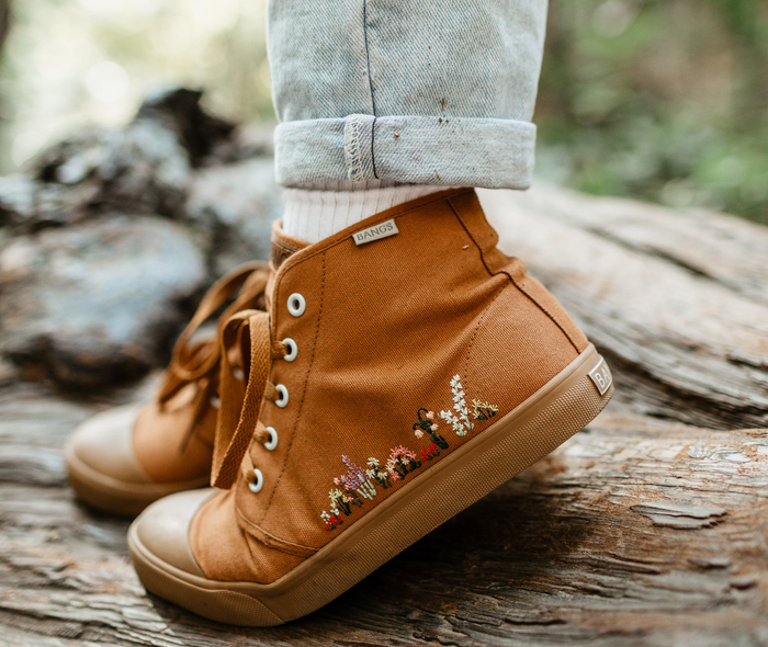 a model sporting tan canvas high-top sneakers with floral embroidery along the sides