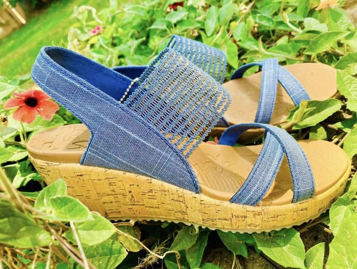 A reviewer's snapshot of the blue wedge sandals placed in a garden bed