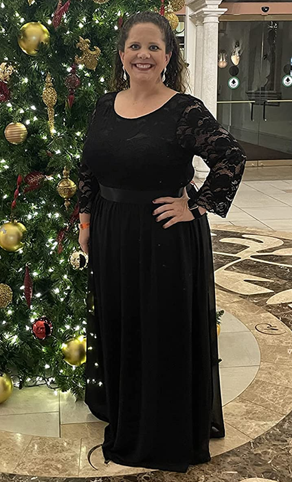 A reviewer in a long black dress posing in front of a Christmas tree