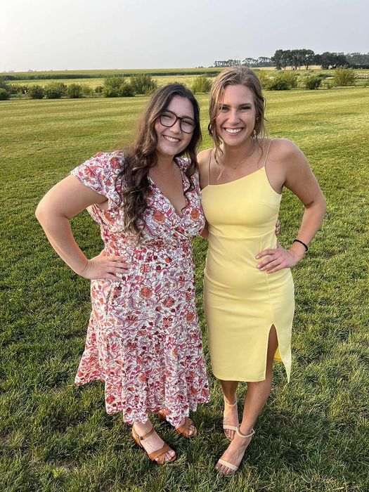 Two reviewers smiling outside, one dressed in a floral print dress and the other in a vibrant yellow slip dress.