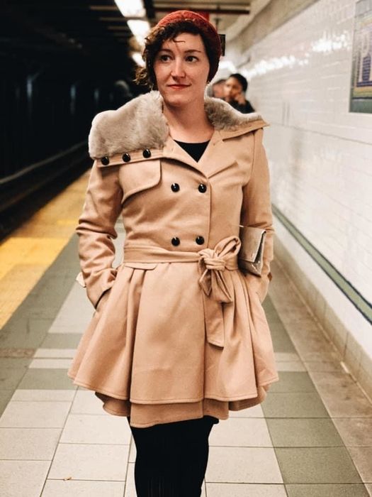 A reviewer showcasing a brown coat paired with black pants