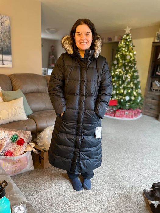 A reviewer showcasing a black coat in a home setting