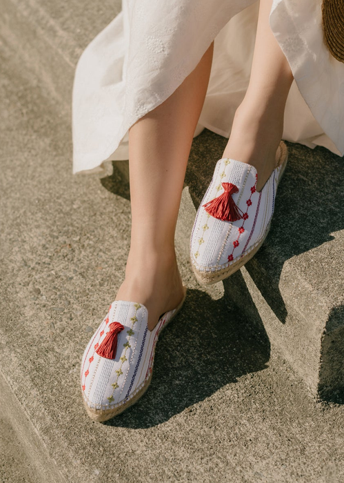 close-up shot of espadrilles crafted from white cotton, adorned with playful red tassels