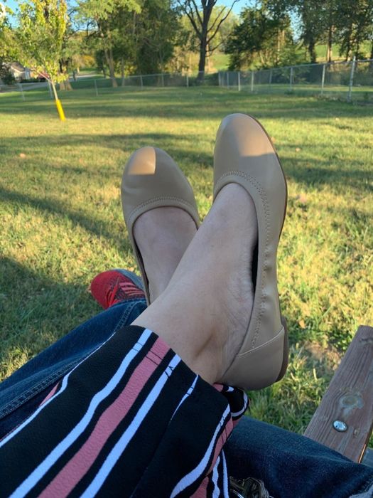 Reviewer sitting outdoors on a bench, wearing beige flats with ankles crossed