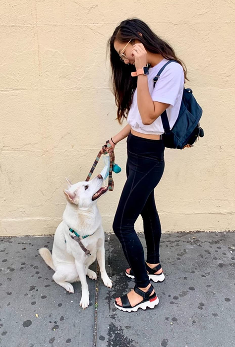 A reviewer pictured standing with their dog, wearing black and white sandals