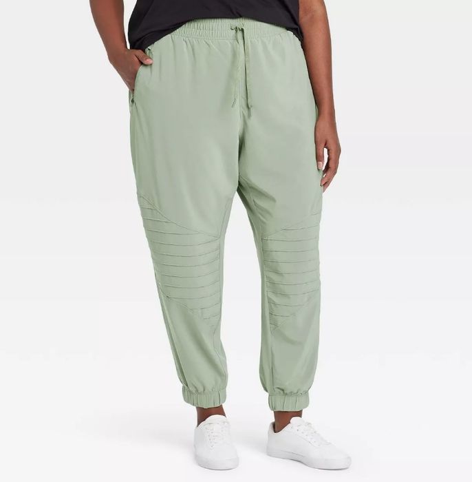 A model wearing a pair of mid-rise stretch woven moto pants in a soft sage color
