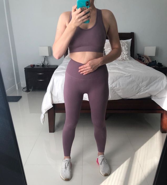 A reviewer wearing a matching purple sports bra and leggings set paired with gray sneakers